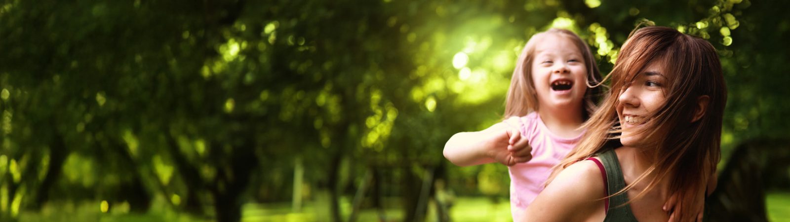 Woman giving a piggyback ride to a laughing child in a sunny, green park.